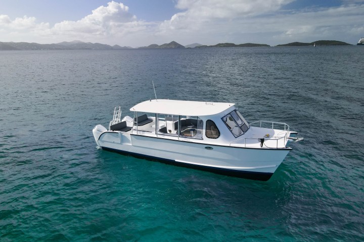 White boat floating on clear blue water with distant hills under a partly cloudy sky.