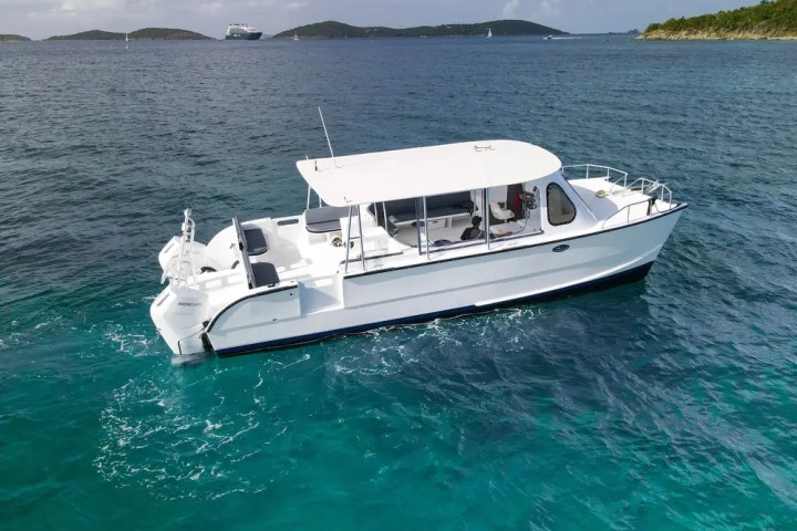 White boat with a canopy floating on turquoise water near small islands.