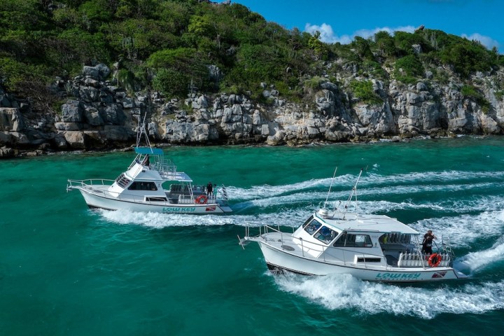 Two boats on clear turquoise water near a rocky, green hillside.