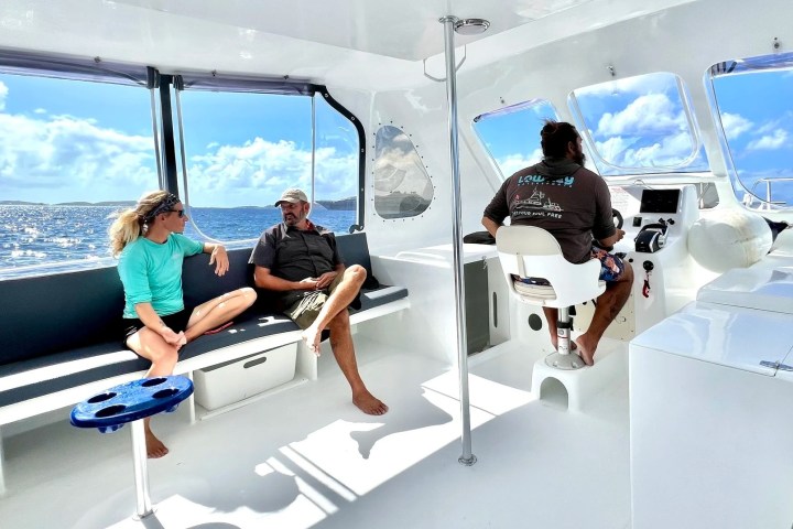 Three people relax on a boat under a sunny sky.