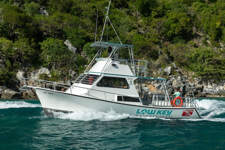 White boat navigating near a rocky, forested shoreline.