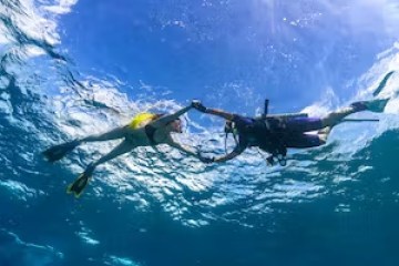 Two scuba divers underwater holding hands surrounded by blue water.