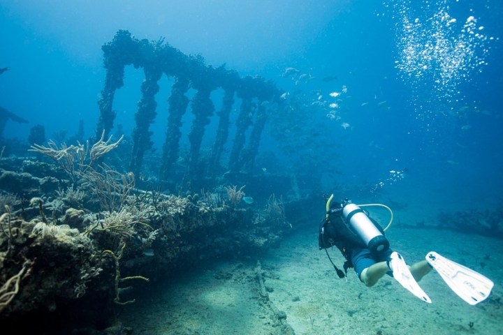Scuba diver exploring an underwater shipwreck with coral growth.